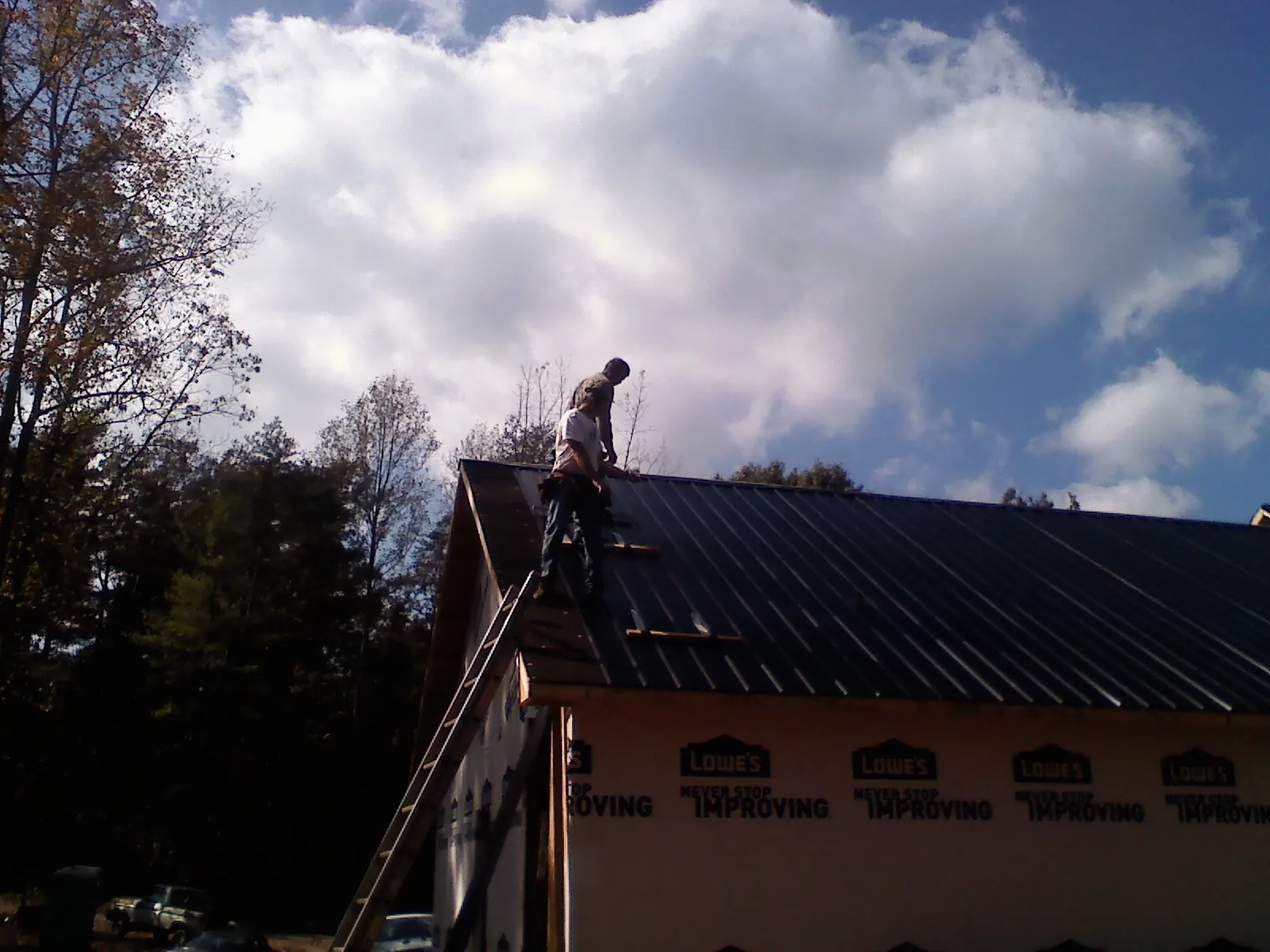 Roofer fastening dark metal panels high against a cloudy sky, from a Roof Inspection job in Allentown