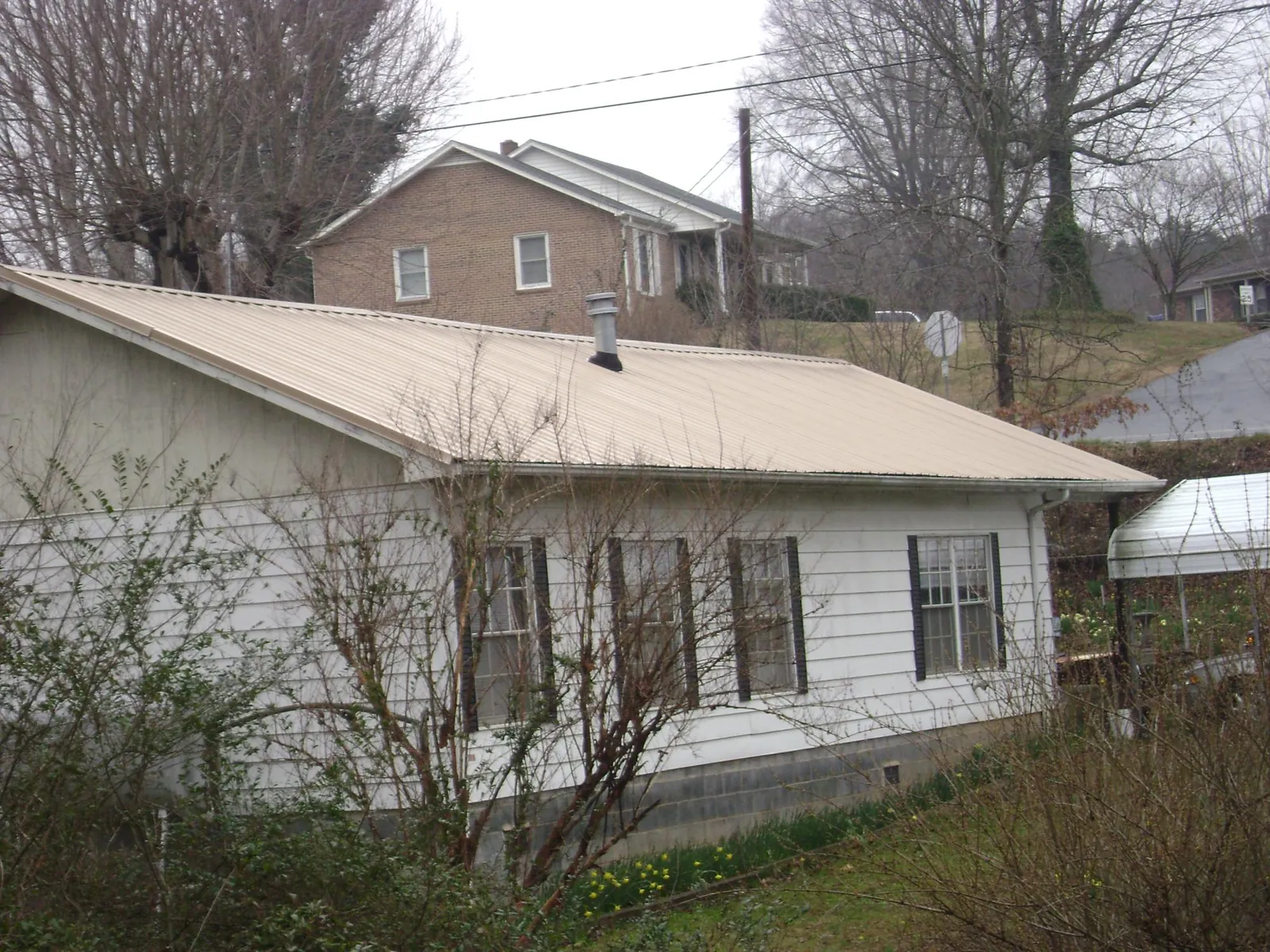 Tan metal roof on a white sided house set into a hillside — Commercial Roofing by Roofing Brothers in Allentown